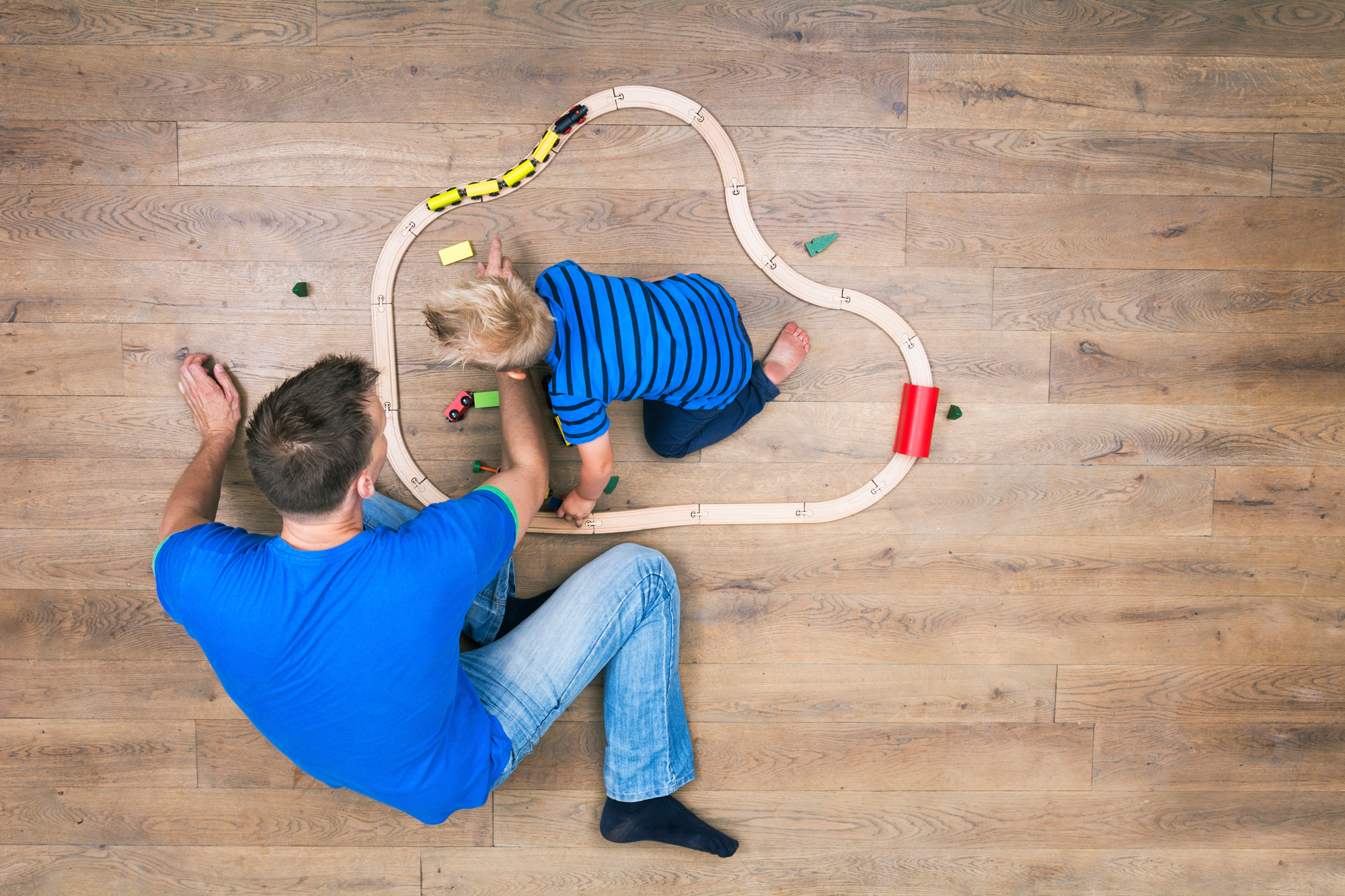 father and son playing with train on wood floor 